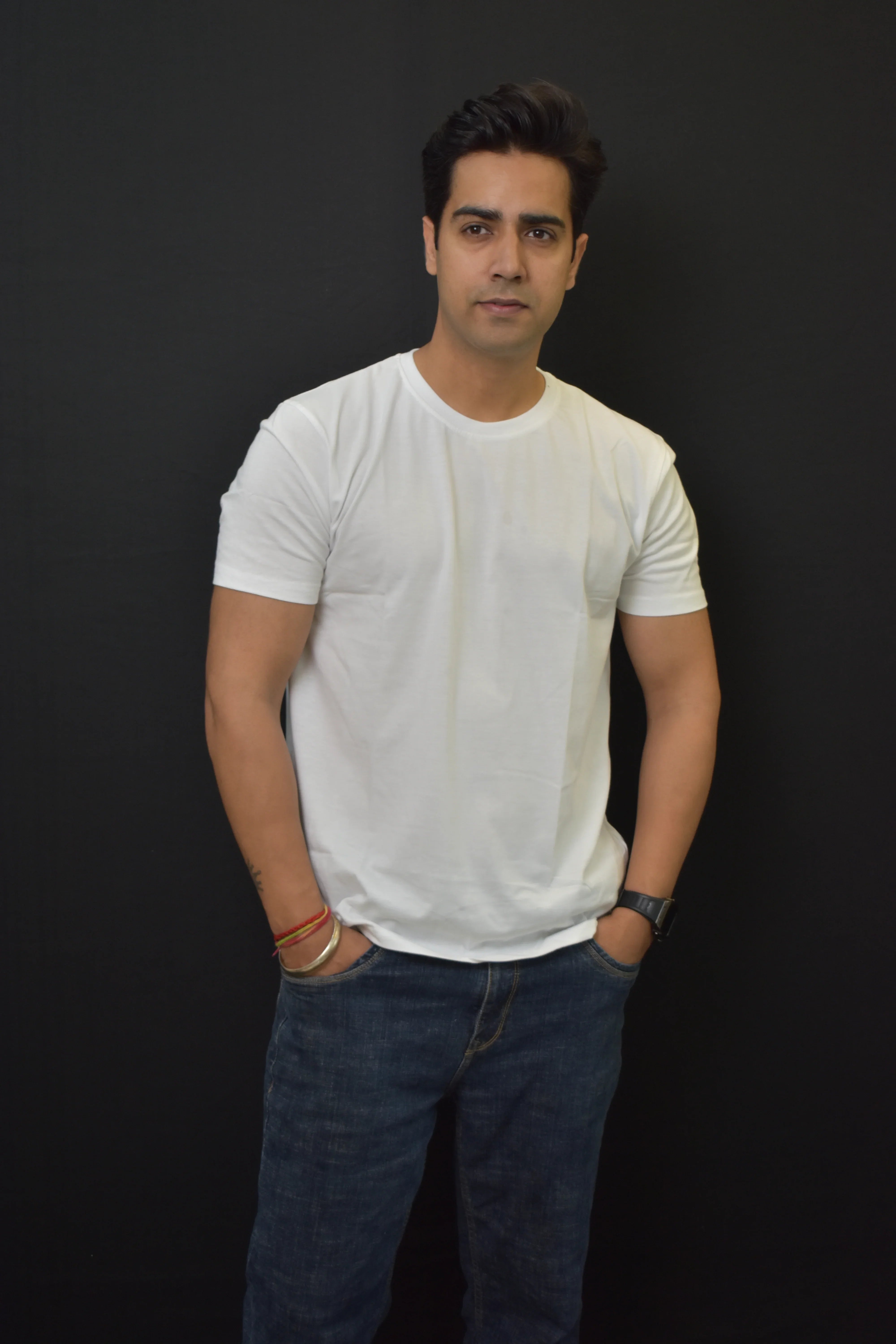 Man wearing a Pavline white t-shirt and blue jeans against a black background