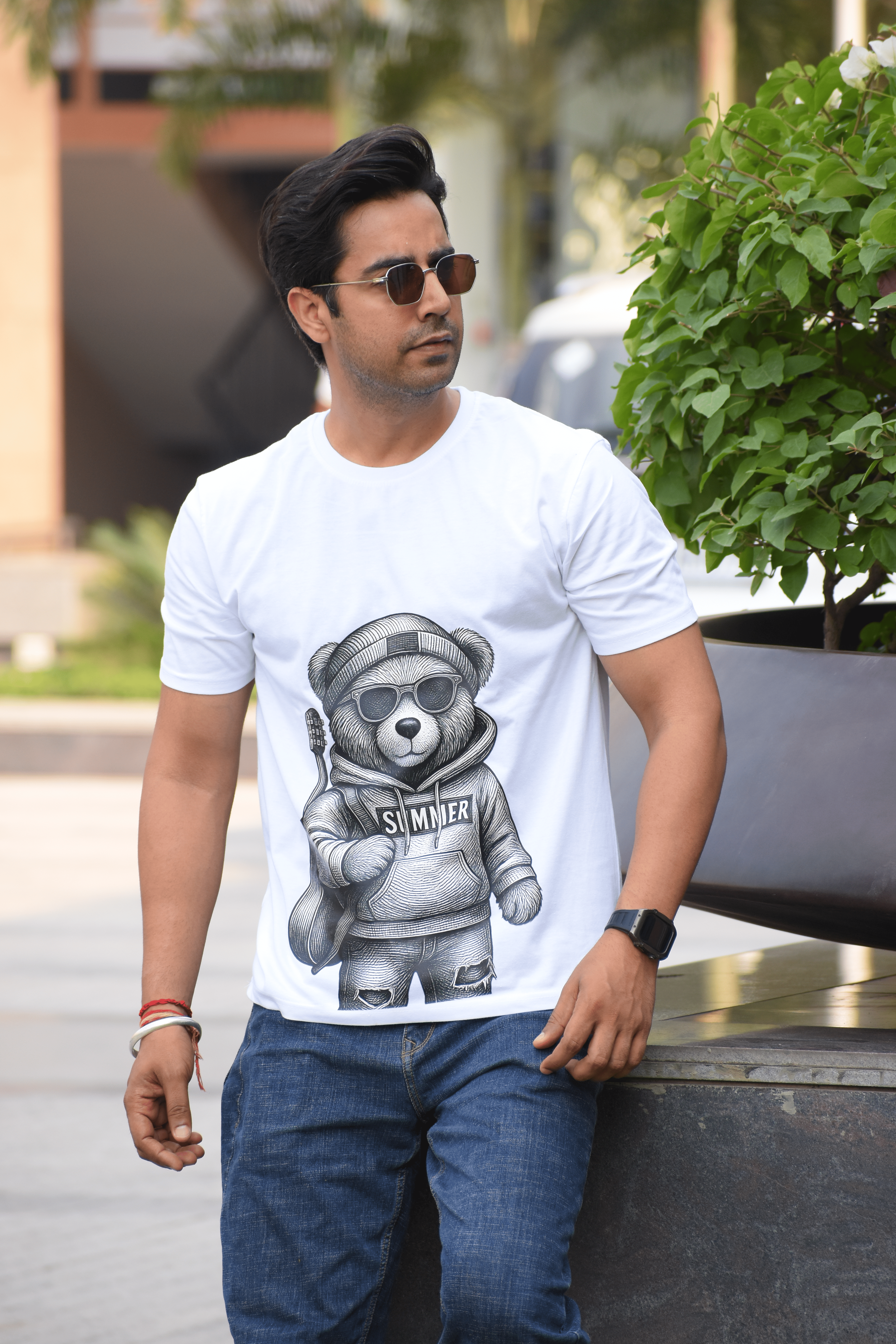 Man wearing a white t-shirt with a bear graphic and sunglasses outdoors.