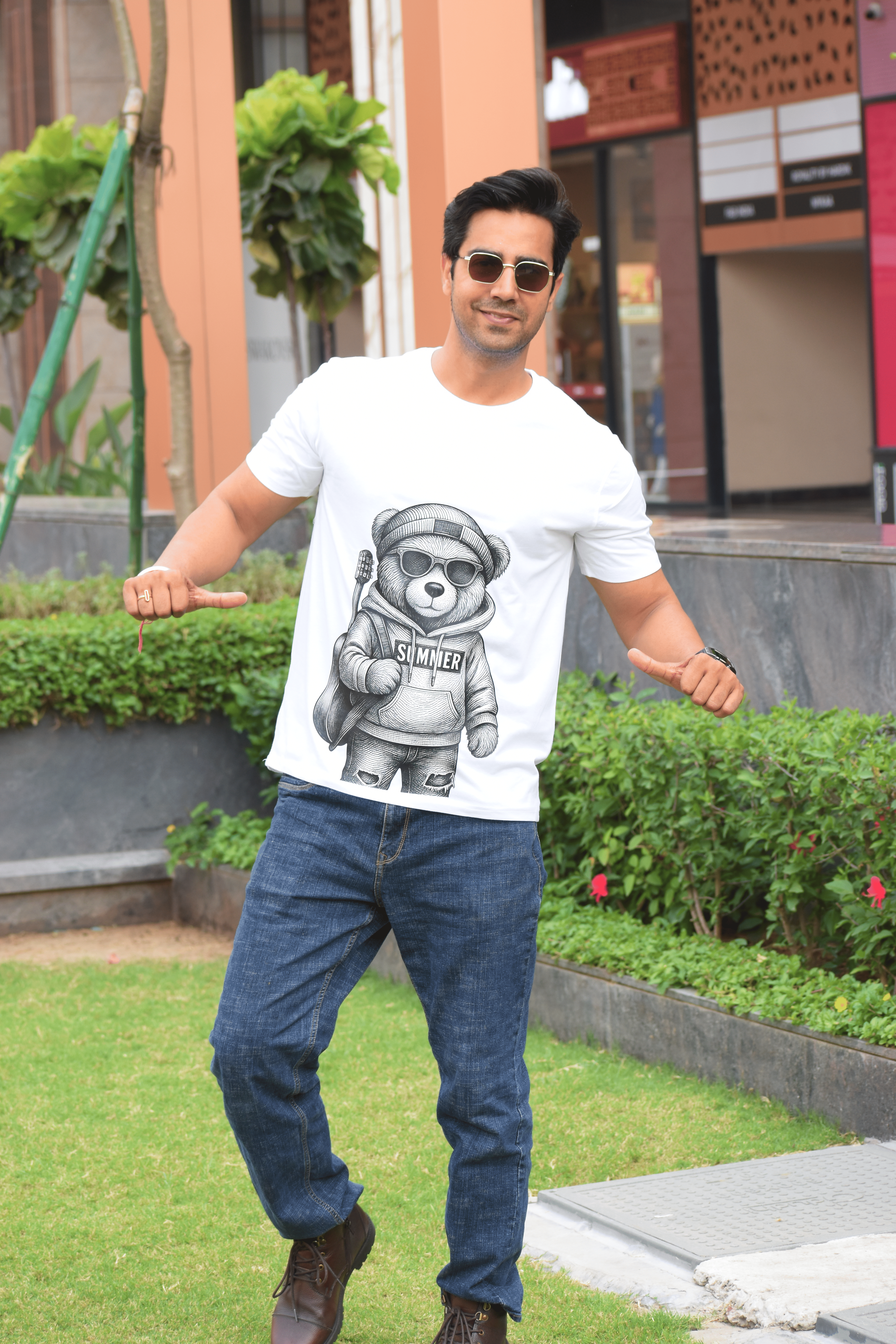 Man wearing a white t-shirt with a graphic design and blue jeans, standing outdoors.
