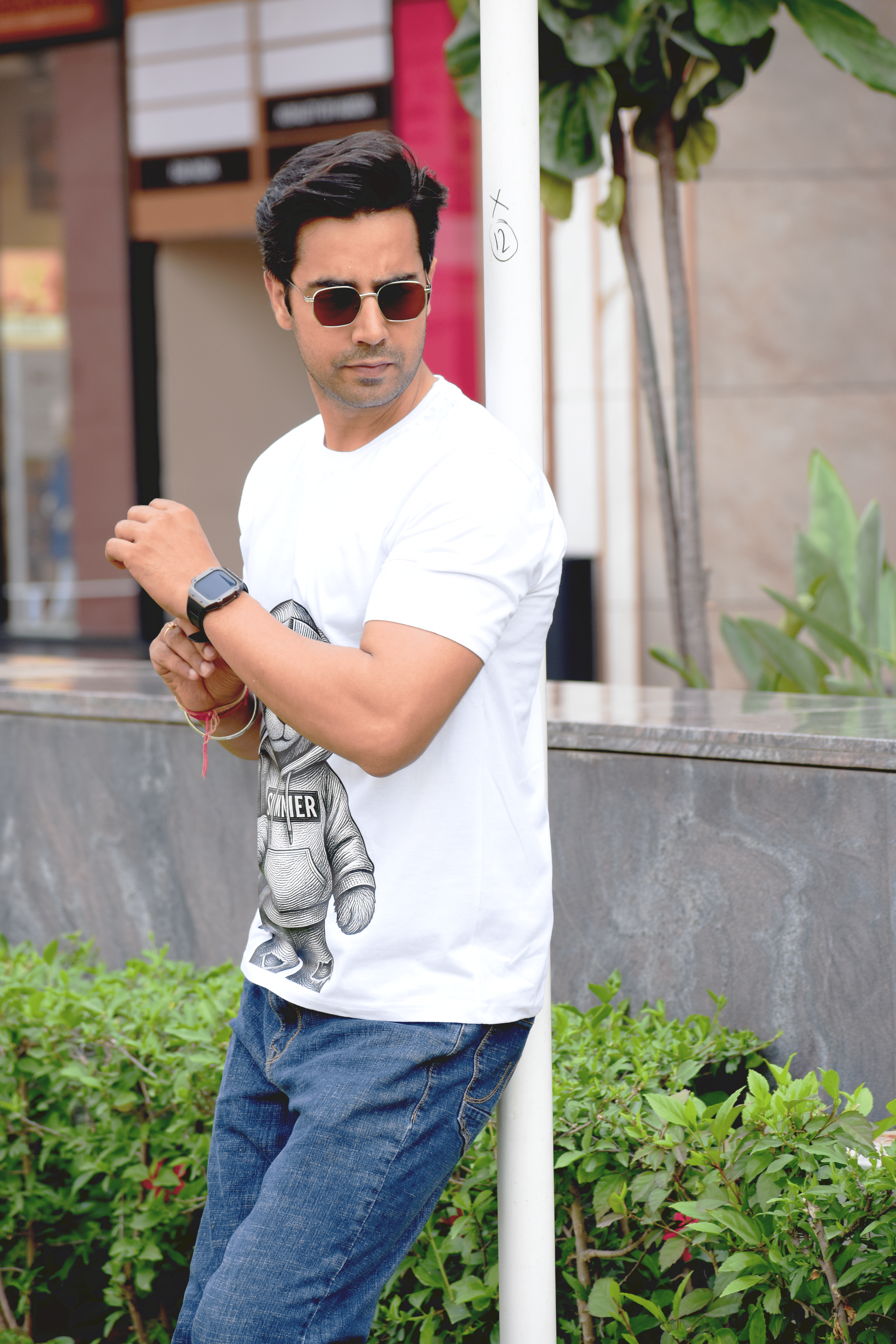 Man wearing a white t-shirt with a graphic design, sunglasses, and a watch outdoors.
